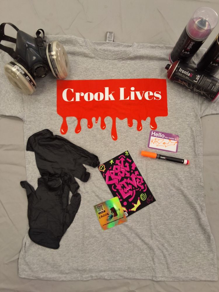 Crook Lives graphic tee flat lay with spray paint cans and a respirator mask