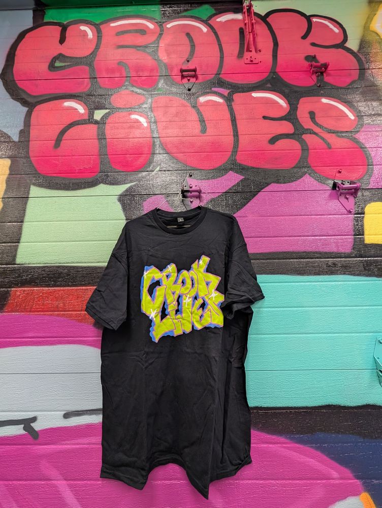 Crook Lives tee hanging in front of a graffiti mural