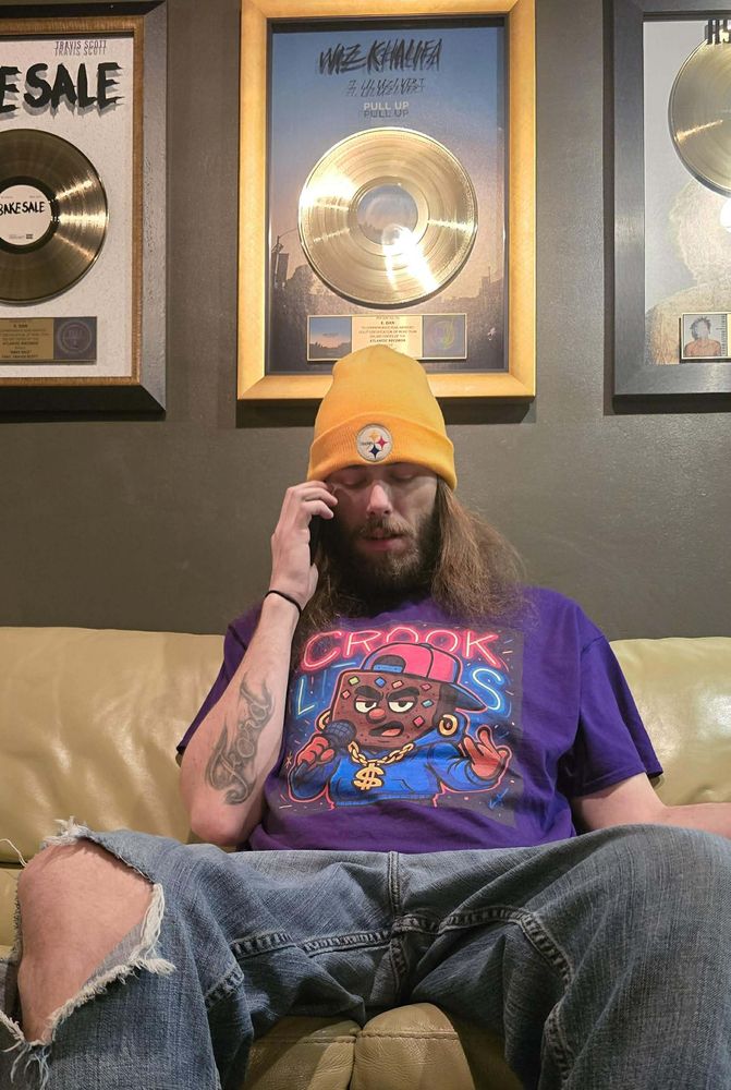 Crook Lives tee worn indoors in front of framed gold records